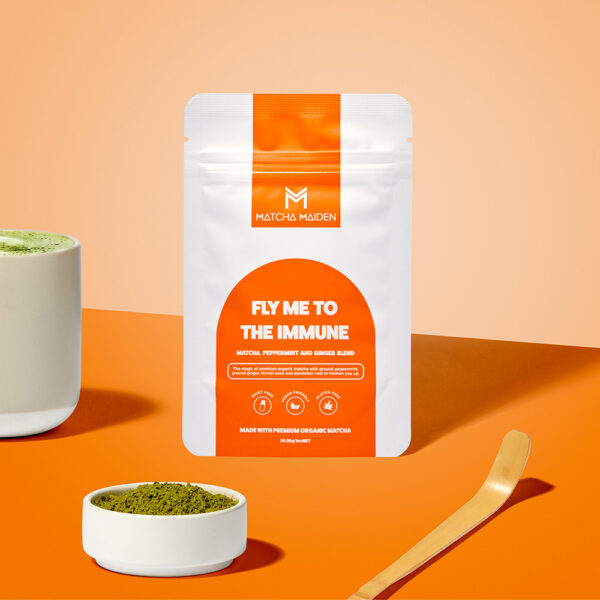 Matcha Maiden Fly Me To The Immune 28.35g pouch on a vibrant orange background with a bamboo scoop and a small bowl of matcha.