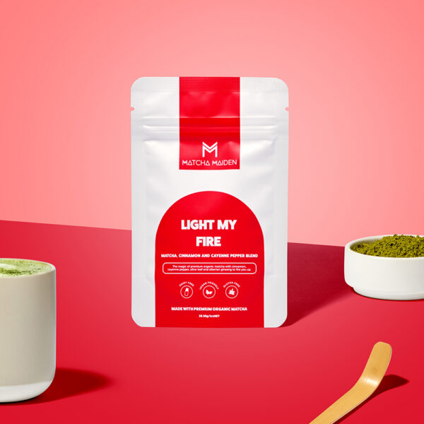 Matcha Maiden Light My Fire 28.35g matcha, cinnamon, and cayenne pepper blend pouch with hot latte, and a bamboo scoop.