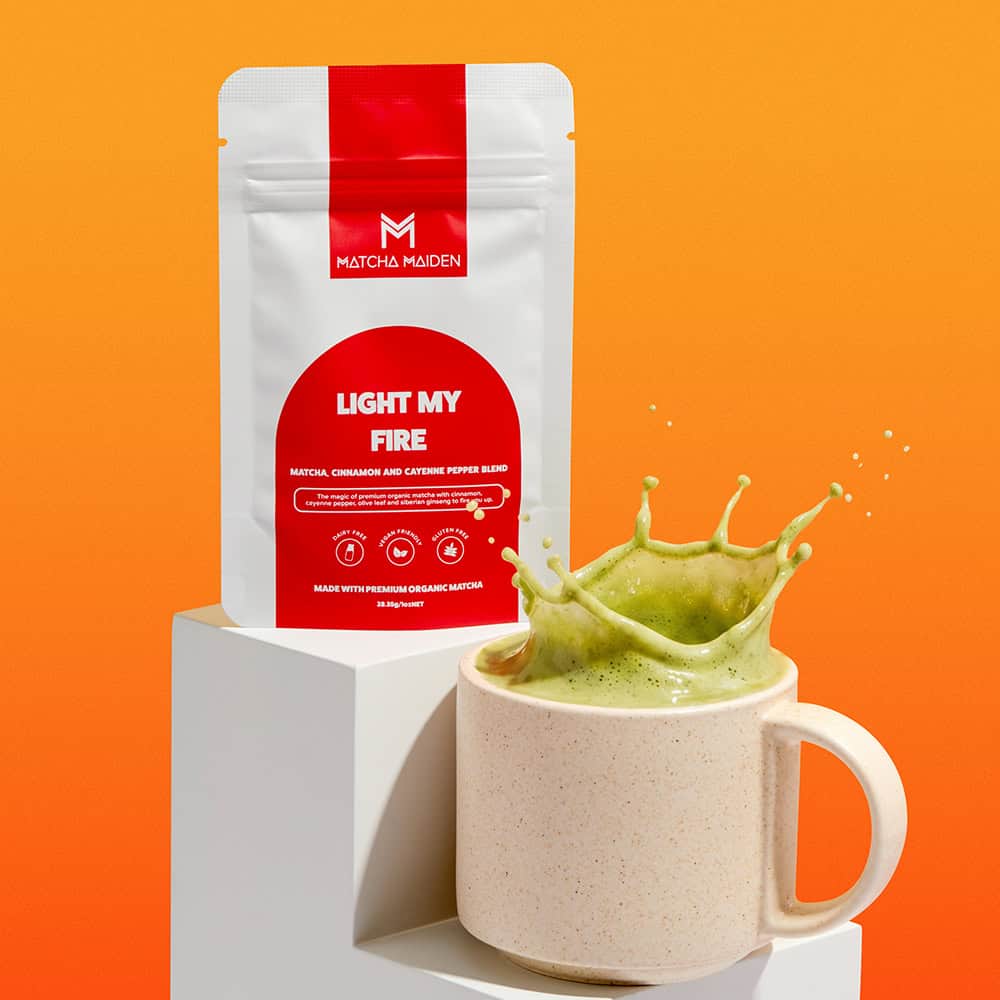 Matcha Maiden Light My Fire matcha, cinnamon, and cayenne pepper blend pouch standing behind a mug with a dynamic splash.