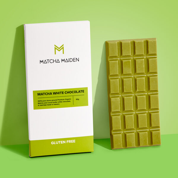 Matcha Maiden 90g Matcha White Chocolate bar leaning against its white and green box packaging on a bright green background.