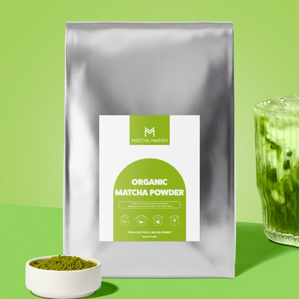 The bulk 1Kg silver pouch of Matcha Maiden Organic Matcha Powder by bowl of matcha and a golden spoon.