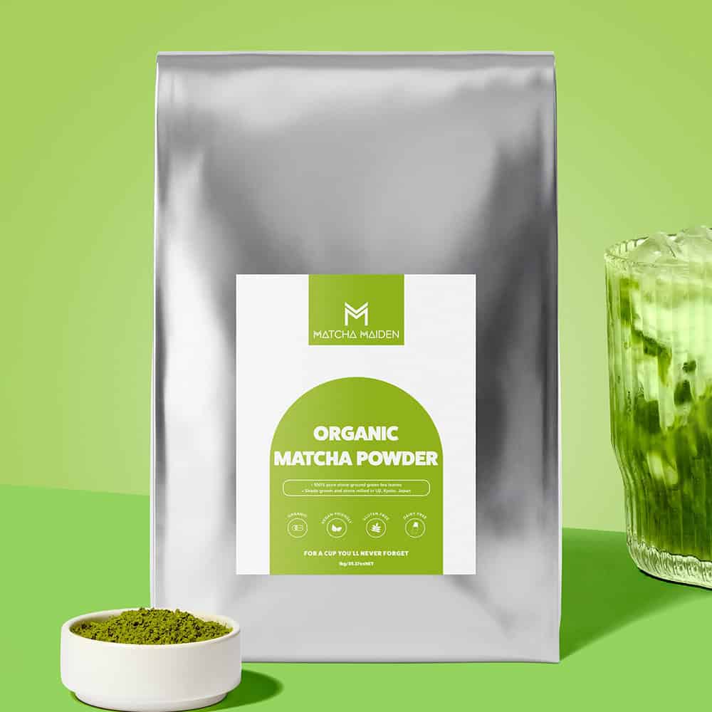 The bulk 1Kg silver pouch of Matcha Maiden Organic Matcha Powder by bowl of matcha and a golden spoon.