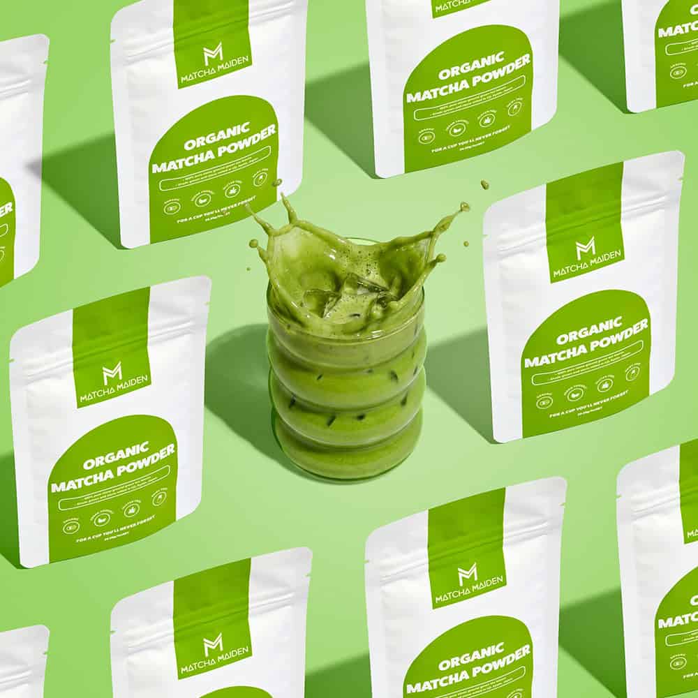 A repeating grid of Matcha Maiden 28.35g organic matcha pouches surrounding a central splashing glass of iced matcha.