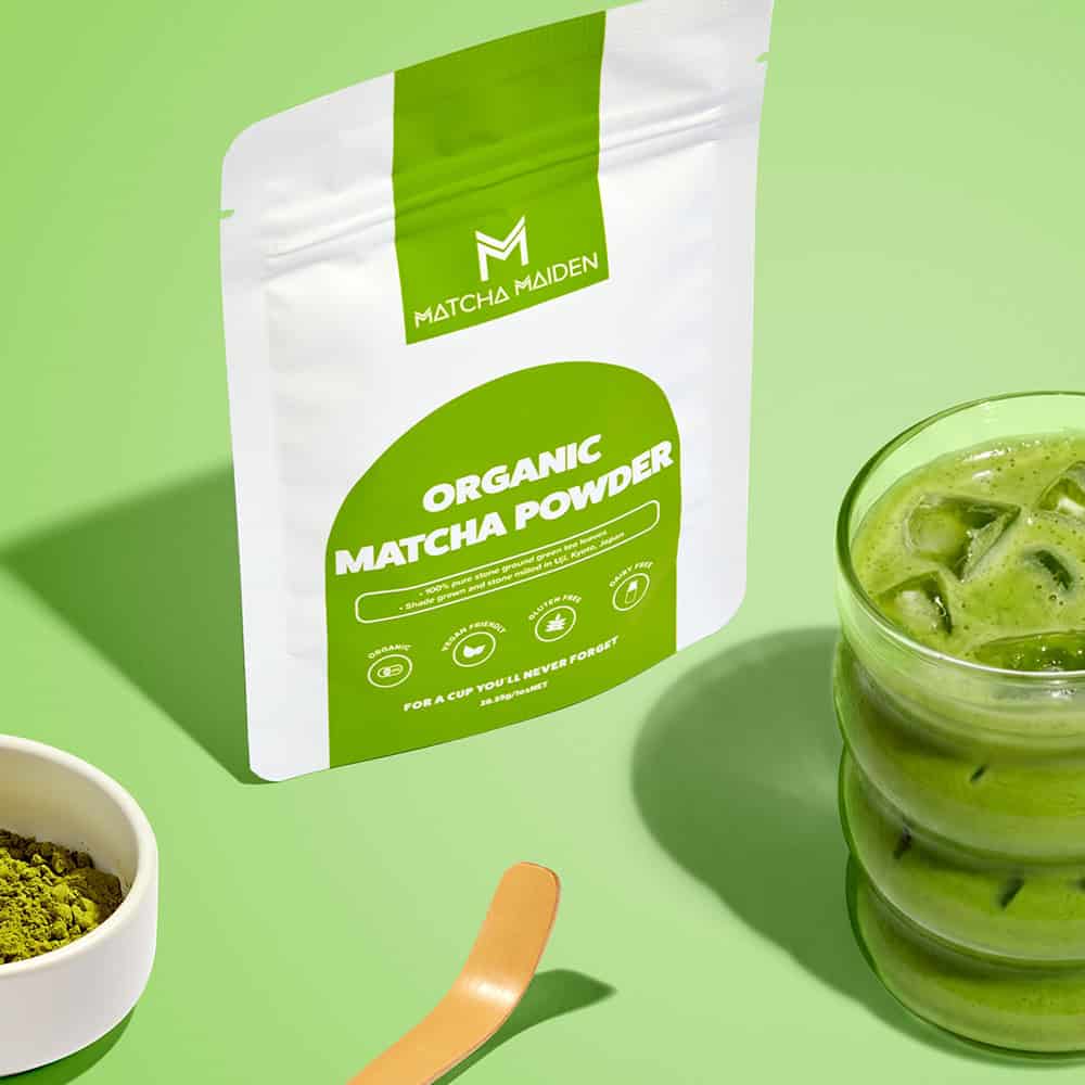 Matcha Maiden 28.35g Organic Matcha pouch on a light green background with refreshing iced matcha latte and a bamboo spoon.