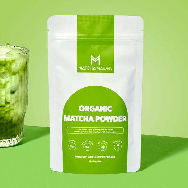 Matcha Maiden 70g organic matcha pouch by glass of iced matcha and a golden spoonful of powder.