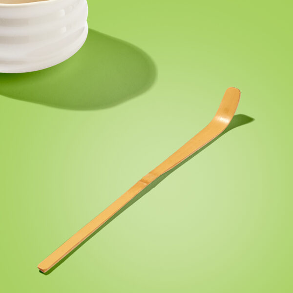 Matcha Maiden traditional bamboo scoop on bright green background by white ceramic bowl.