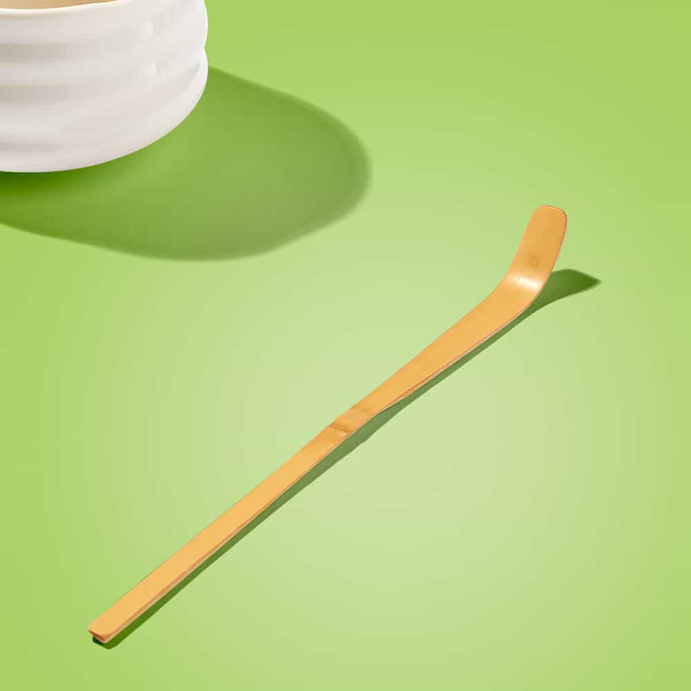 Matcha Maiden traditional bamboo scoop on bright green background by white ceramic bowl.