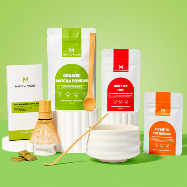 Matcha Maiden Ultimat-cha Bundle displayed on white pedestals against a green background, featuring Organic Matcha, Light My Fire, Fly me to the Immune and Matcha White Chocolate.