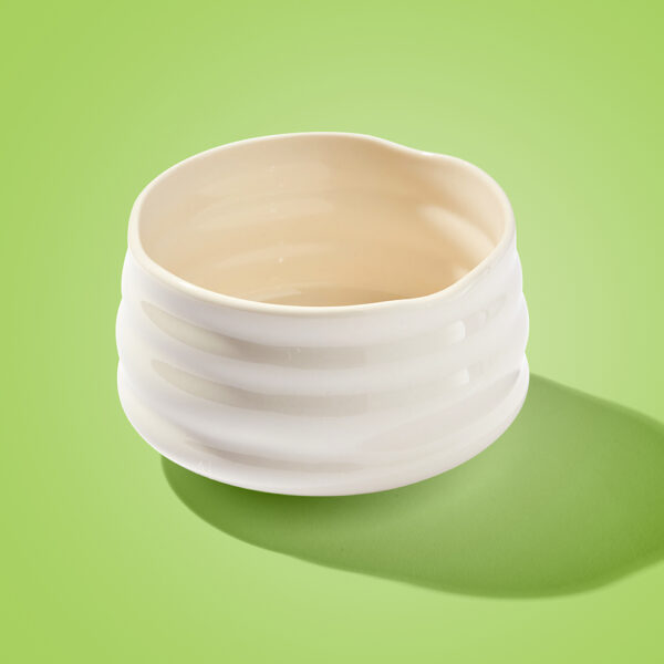 Empty white ceramic matcha tea bowl with a ridged texture, traditionally known as a chawan, on bright green background.