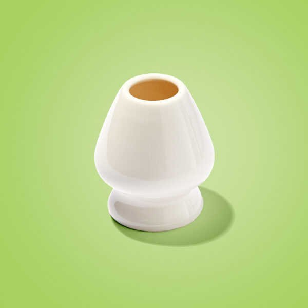 Empty white ceramic matcha whisk holder, known as a kusenaoshi, standing on a bright green background.