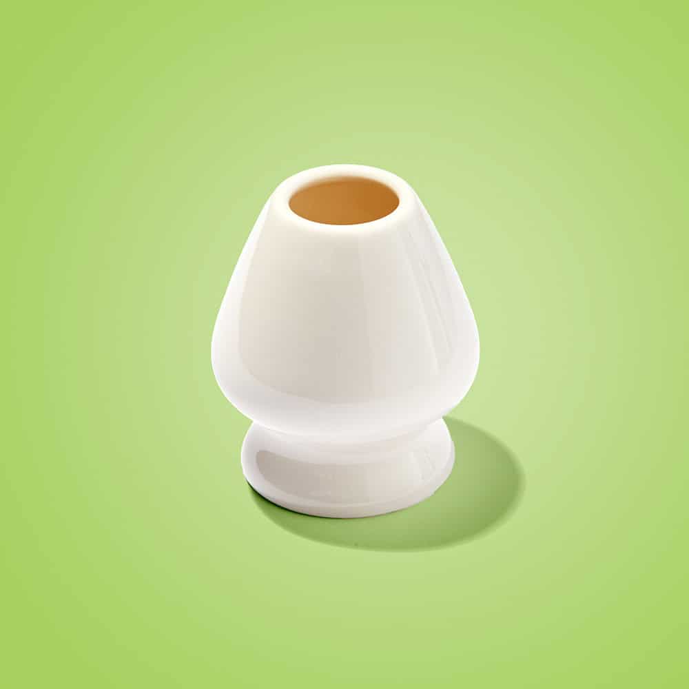 Empty white ceramic matcha whisk holder, known as a kusenaoshi, standing on a bright green background.