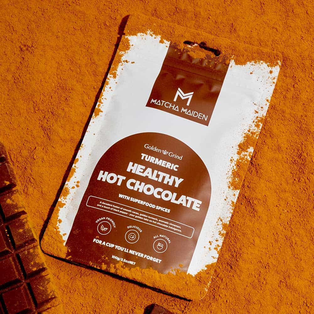 Golden Grind Turmeric Healthy Hot Chocolate 100g pouch lying flat on a rich bed of blended turmeric and cacao powder.