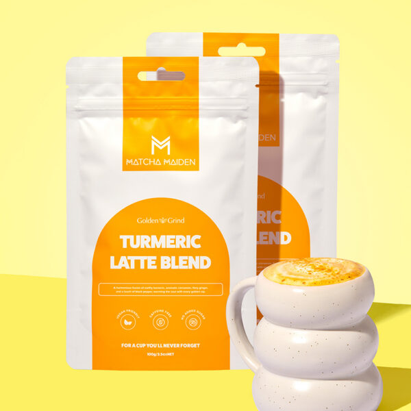 Matcha Maiden Golden Grind Turmeric Latte Blend Combo with 2 100g pouches by white ribbed mug of golden latte and a cinnamon stick.