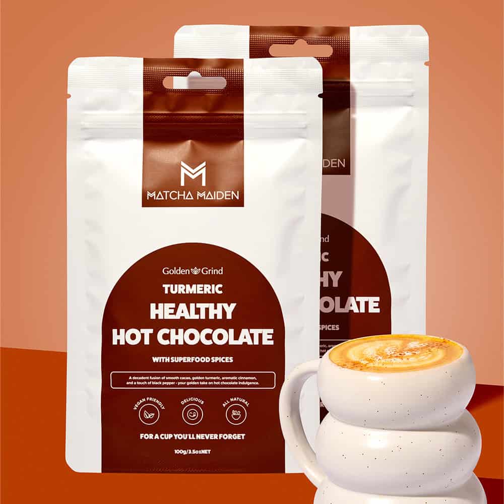 Matcha Maiden Golden Grind Turmeric Hot Chocolate Blend Combo with 2 x 100g pouches by warm ribbed mug of hot chocolate.