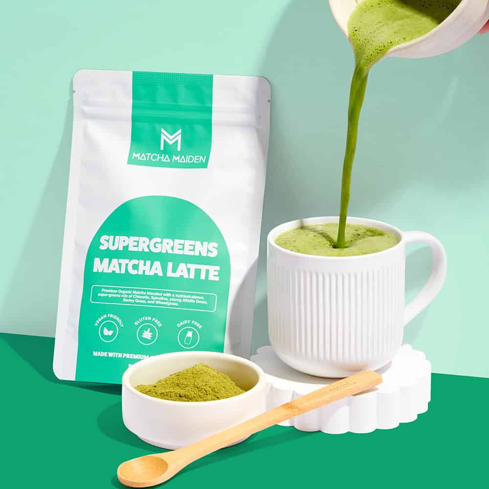 Pouring a fresh hot matcha latte into a white ribbed mug by Matcha Maiden Supergreens Matcha Latte 150g pouch.