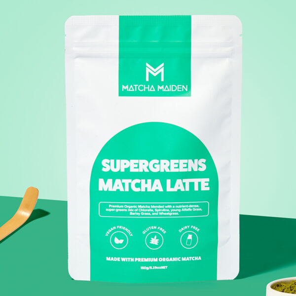 Matcha Maiden Supergreens Matcha Latte 150g pouch by a bamboo scoop and a bowl of green powder on a vibrant teal background.