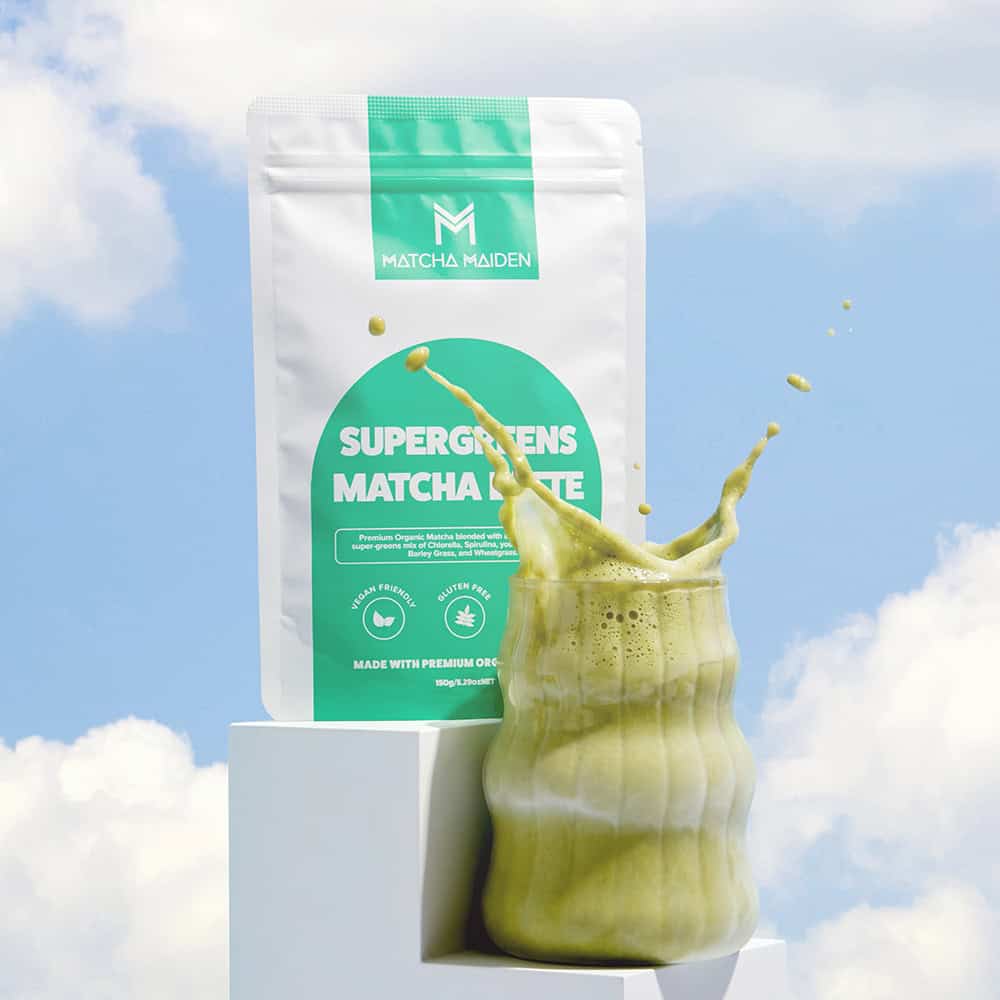 Matcha Maiden Supergreens Matcha Latte 150g pouch displayed on white pedestals behind a ribbed glass.