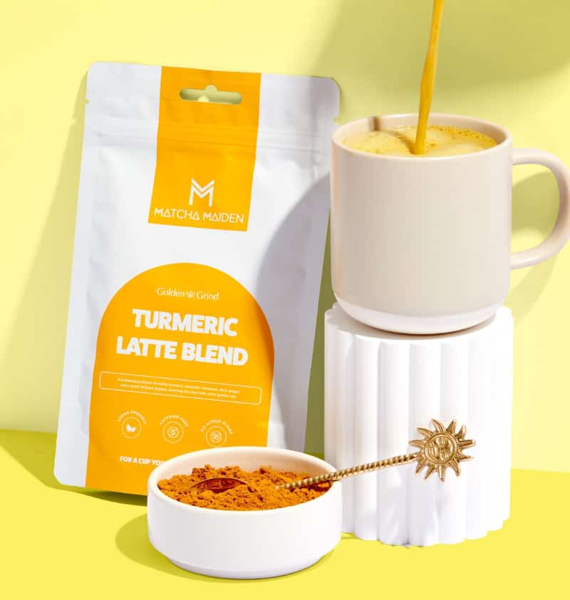 Matcha Maiden Turmeric Latte Blend pouch and a white mug with a splashing golden latte against a blue sky.